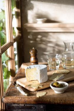 a wooden table topped with cheese and crackers next to a glass vase filled with water