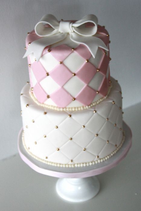 a three tiered cake decorated with pink and white squares, bows, and pearls