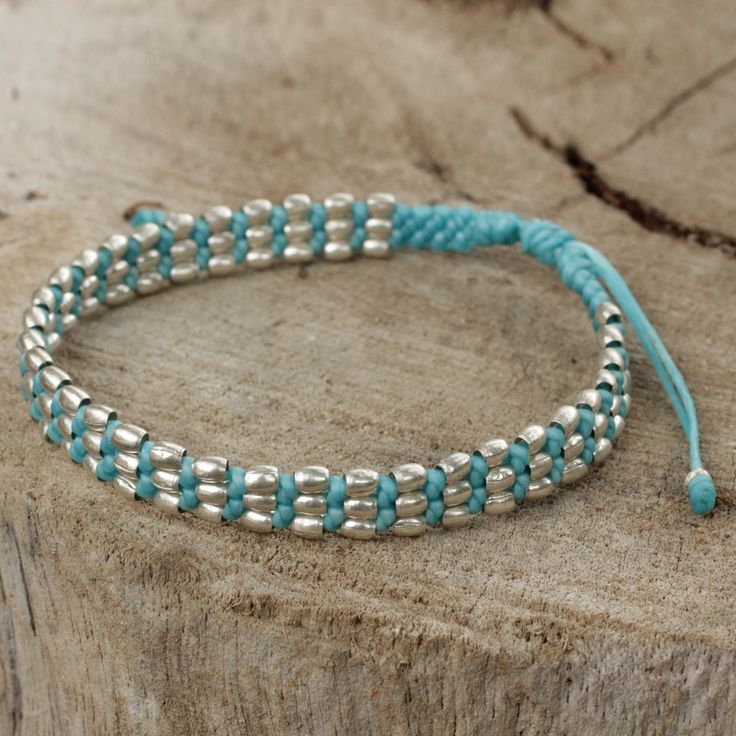 a close up of a bracelet on a piece of wood with blue string and silver beads