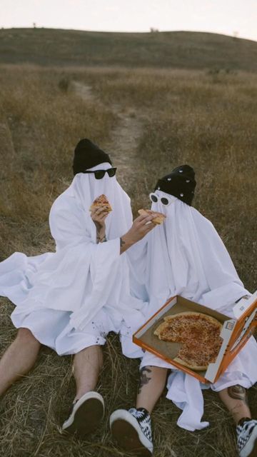 two people in white robes eating pizza and sitting on the ground with their eyes closed