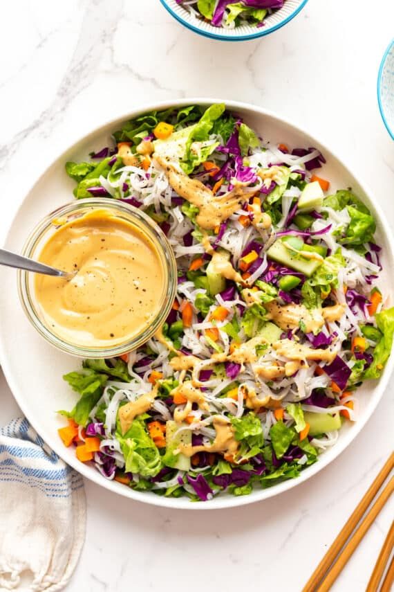 a white plate topped with a salad covered in dressing next to two bowls filled with lettuce and carrots