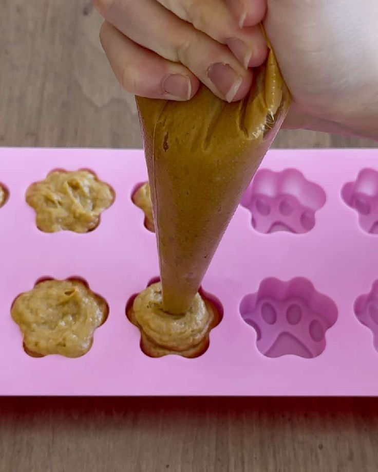 a person is dipping peanut butter into some cookie dough on a pink tray with paw prints