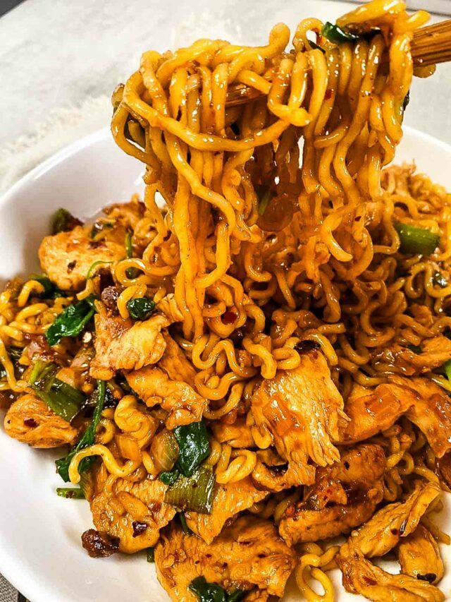 noodles with meat and vegetables being lifted by chopsticks from a white plate on a table