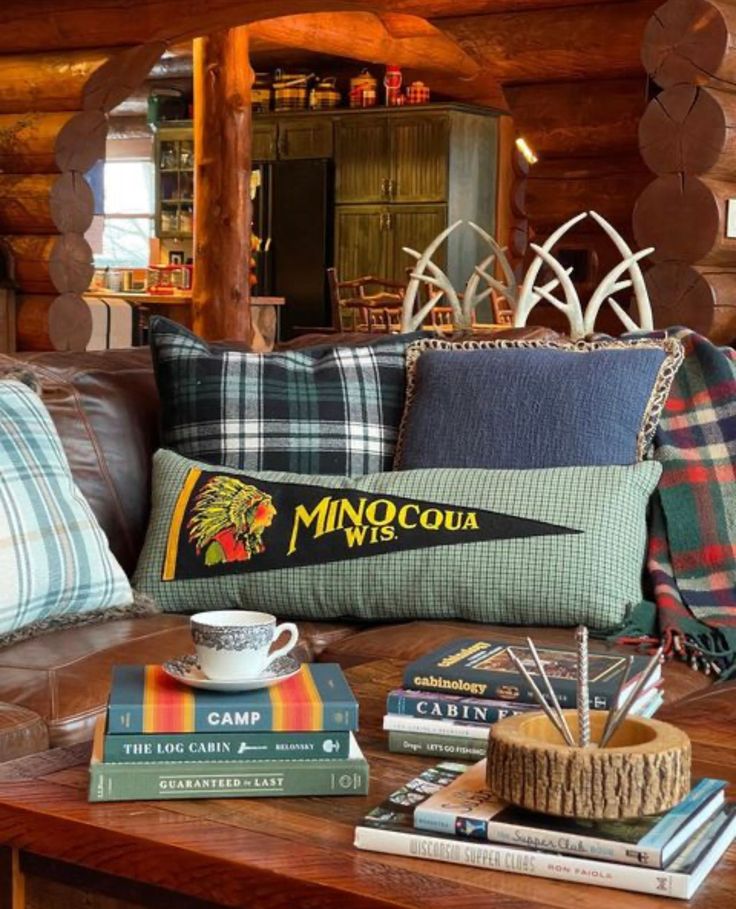 a coffee table topped with books next to a couch covered in plaid pillows and blankets