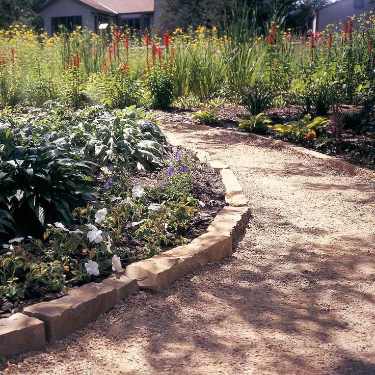 a garden with various plants and flowers in the dirt path leading to a house on top of a hill