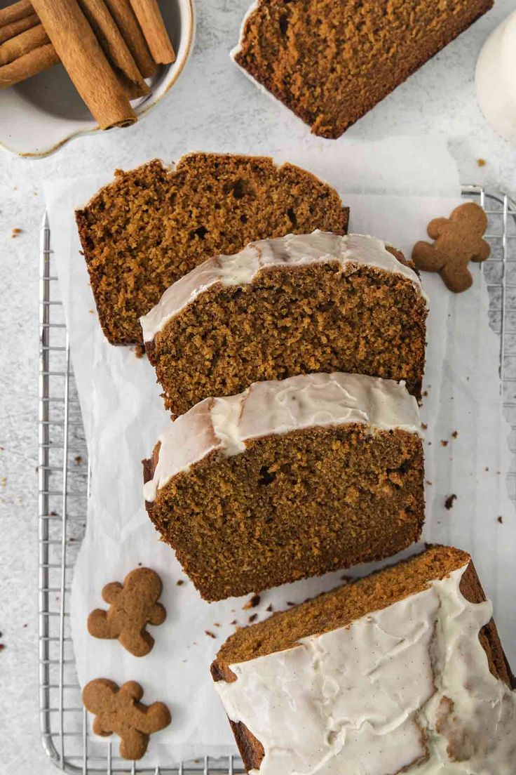 slices of gingerbread bread with icing on a cooling rack next to cinnamon sticks