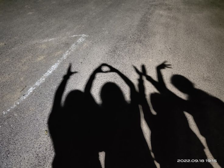 the shadow of three people holding hands up in the air on an empty asphalt road