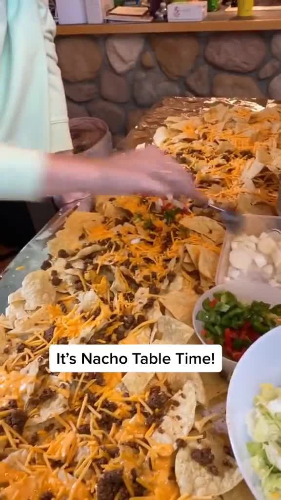 a table full of nachos and other food with the caption it's nacho table time