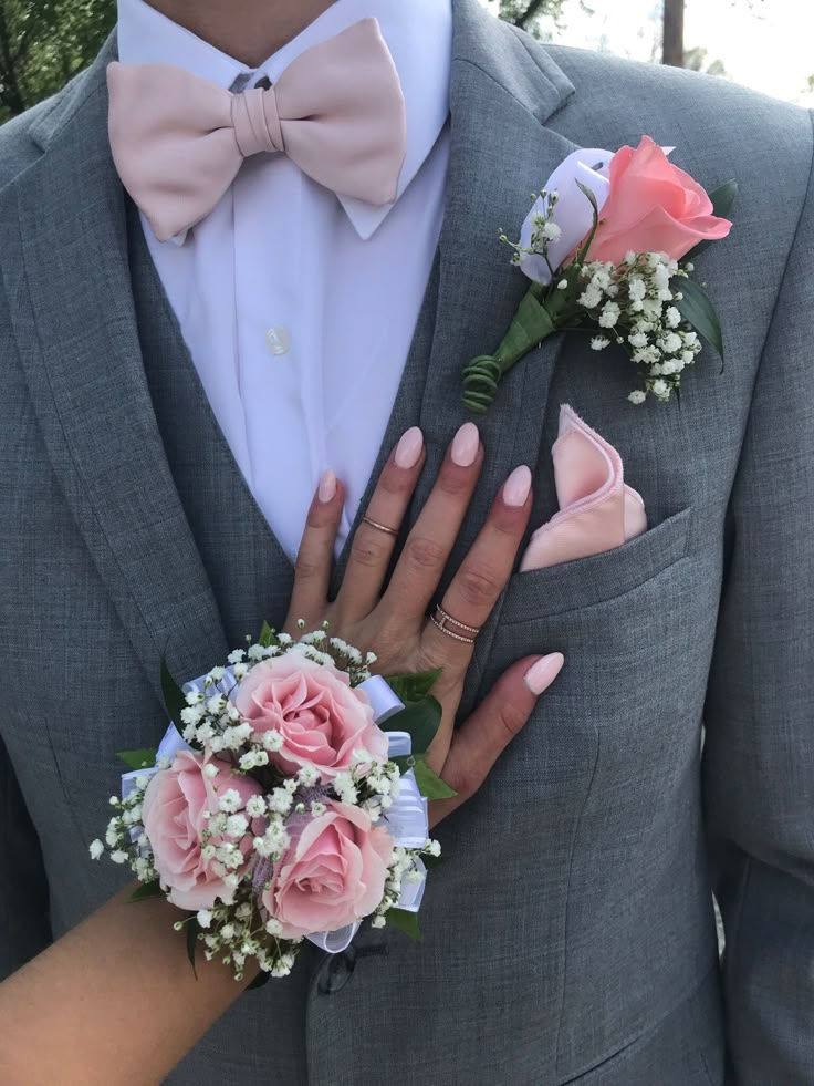 a man in a gray suit and pink flowers with his hands on the woman's lapel