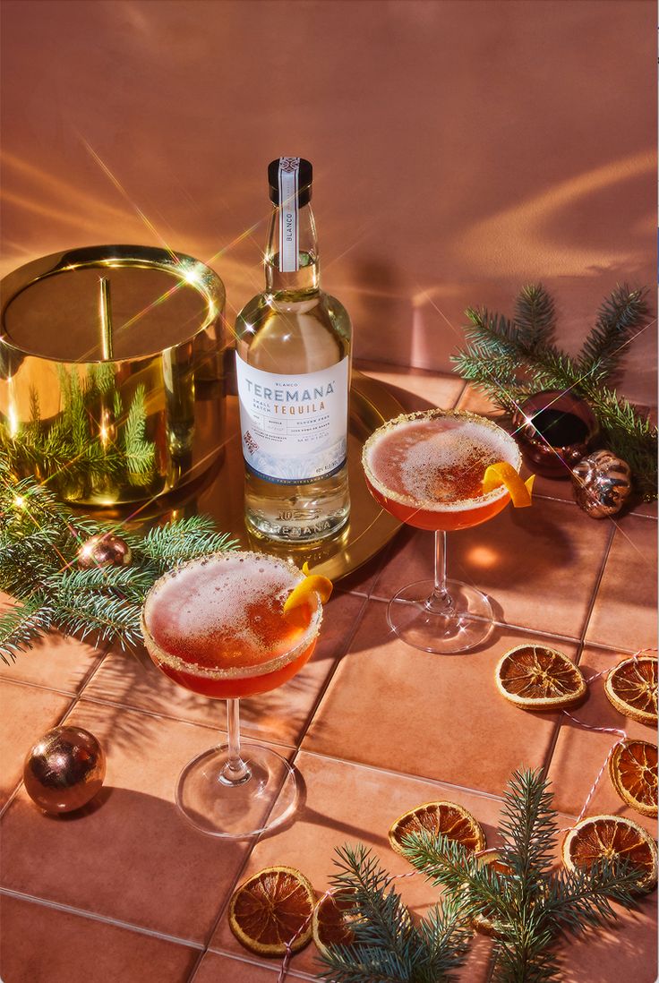 two wine glasses filled with oranges on a table next to a bottle of booze