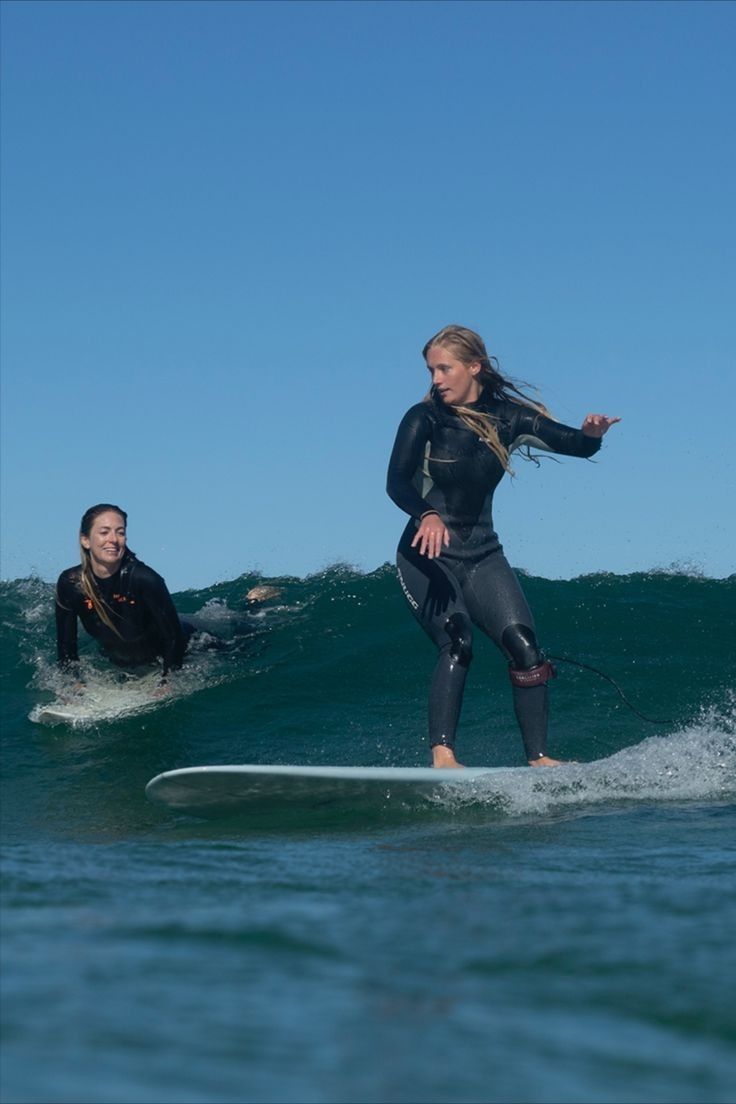 two people on surfboards in the ocean, one riding a wave while another watches