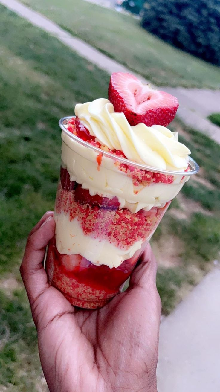 a person holding up a dessert with strawberries and cream in it's cup