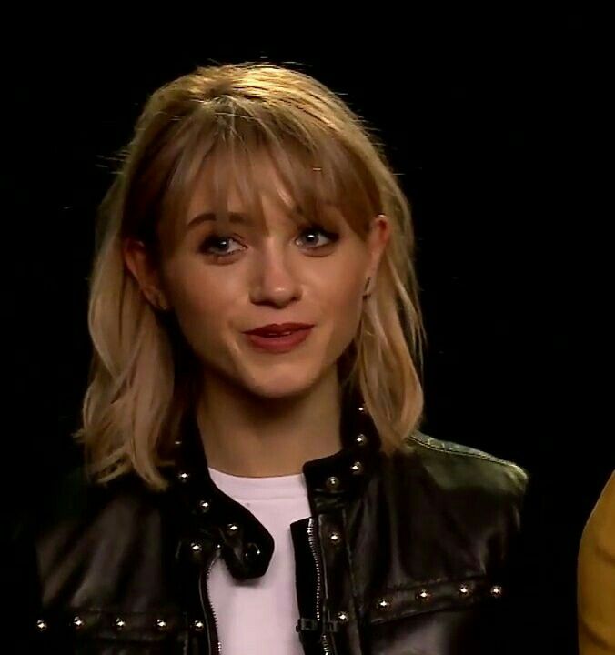 a close up of a person wearing a black jacket and white t - shirt with blonde hair