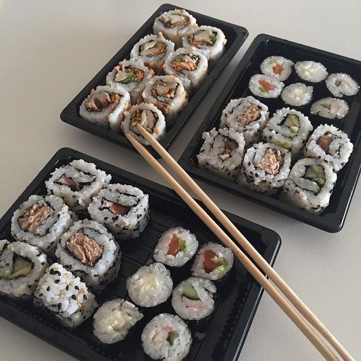 three trays filled with sushi and chopsticks on top of a table