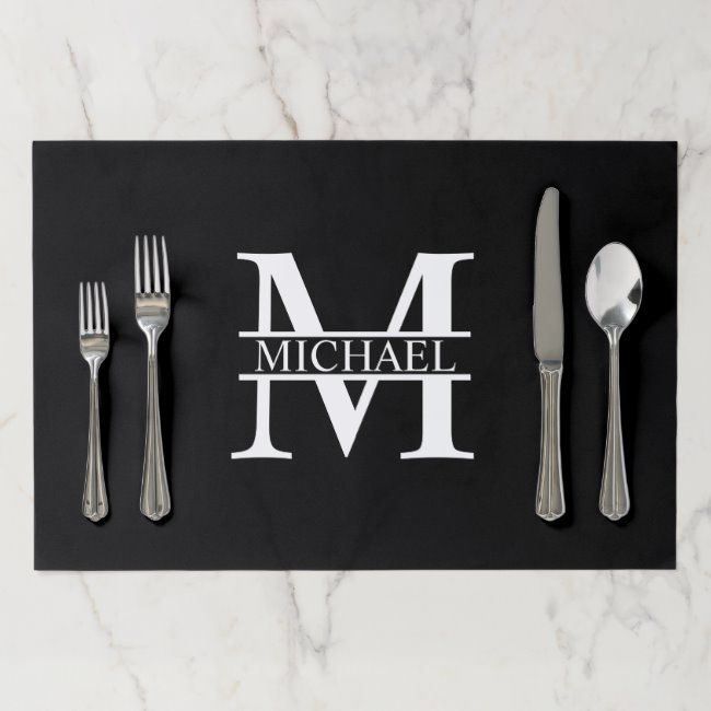 a black place mat with the letter m on it and silver utensils next to it