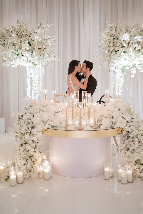 a newly married couple kissing in front of a wedding cake surrounded by flowers and candles