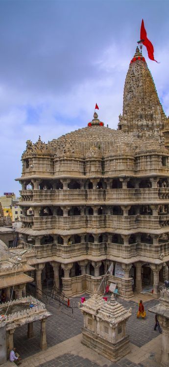 an elaborately carved building with flags flying in the air and people walking around it