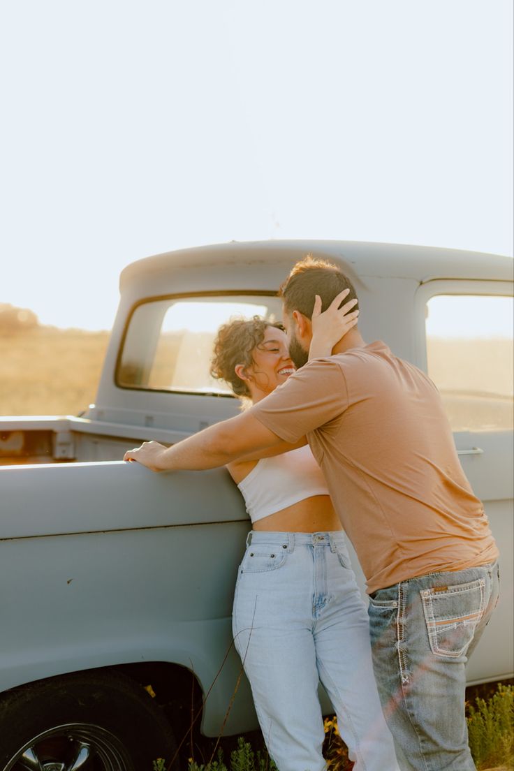 a man and woman leaning against the back of an old pick up truck in a field