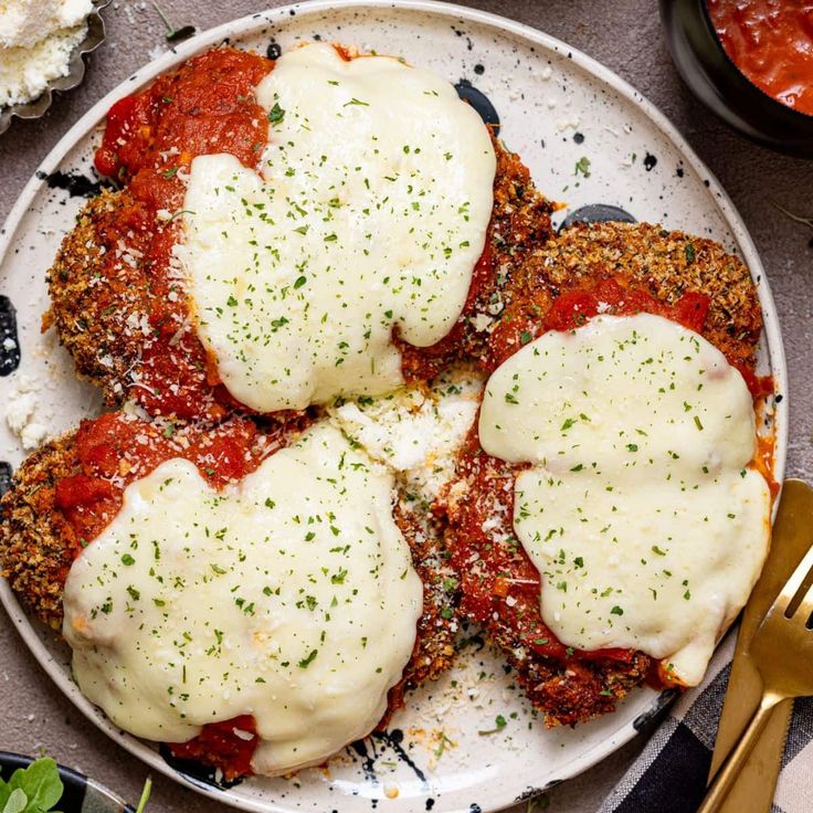 three meat patties covered in sauce and cheese on a white plate with gold utensils