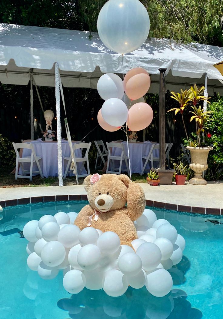 a teddy bear sitting in the middle of a pool surrounded by balloons