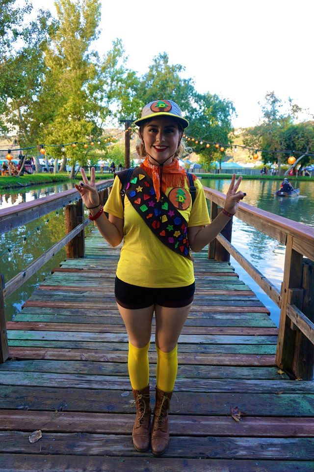 a woman in yellow shirt and black shorts standing on a wooden bridge with her hands up