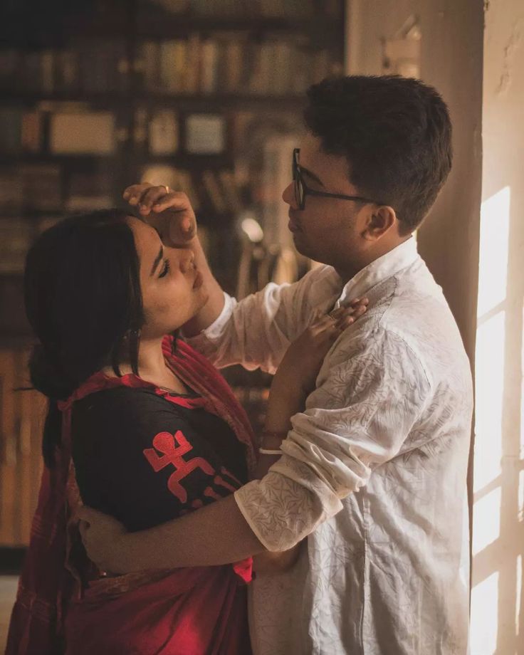 a man and woman standing next to each other in front of a bookshelf