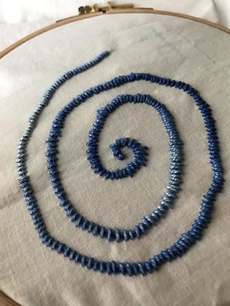 a close up of a blue beaded necklace on a white cloth with a wooden hoop