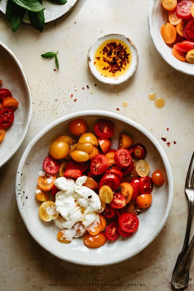 two white bowls filled with different types of tomatoes and other vegetables on top of a table