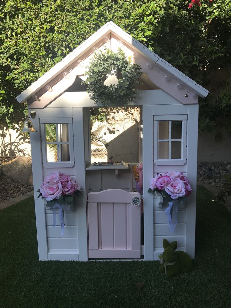 a small white doll house with pink flowers in the front and side windows on top