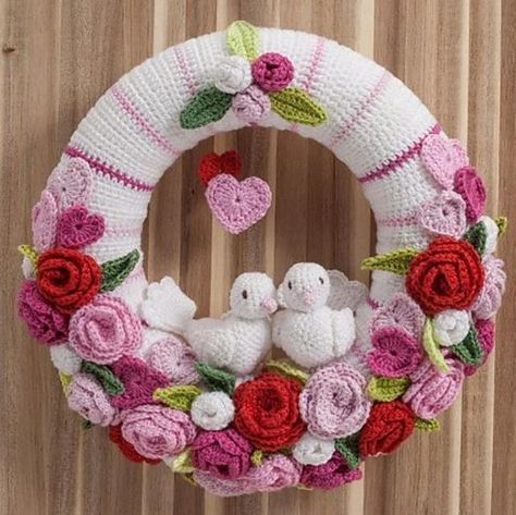 a crocheted wreath with two white doves and roses on it, hanging from a wooden wall