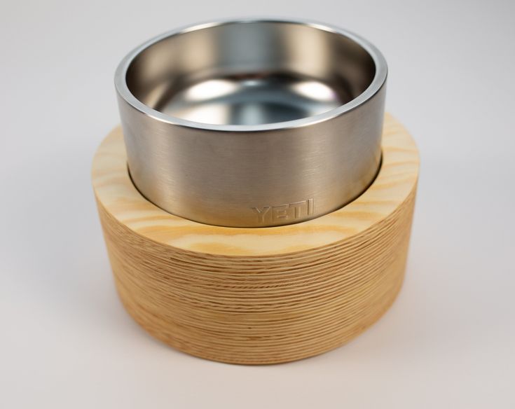 a stainless steel bowl sitting on top of a wooden stand next to a white background