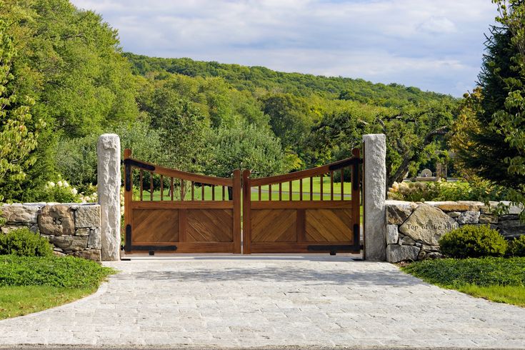 a gated driveway with stone walls and trees in the background