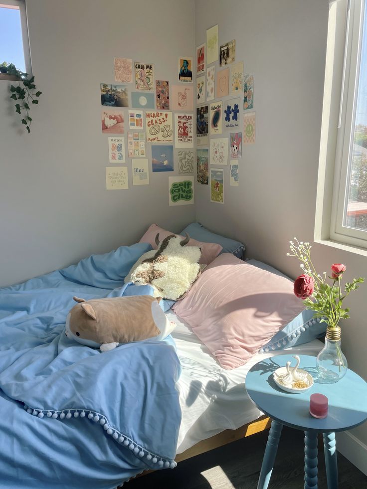 a bed with blue sheets and pillows in a room next to a table with flowers on it