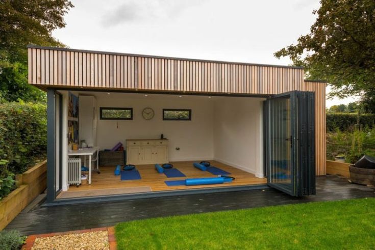 an outdoor room with yoga mats on the floor and wooden walls, surrounded by green grass