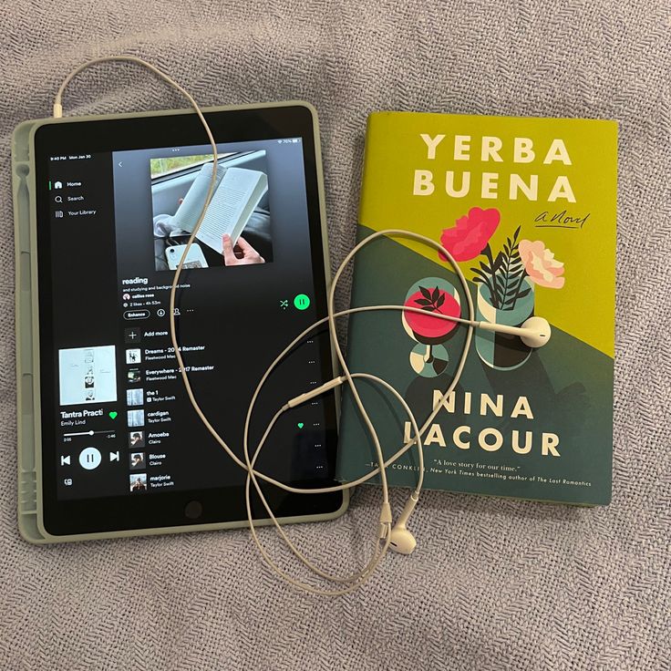 there is a book and headphones on the bed next to this electronic device,