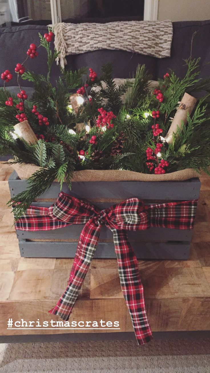 a christmas centerpiece with pine branches, holly and red berries in a wooden crate