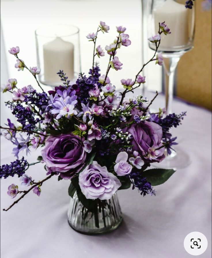 a vase filled with purple flowers on top of a table next to two white candles