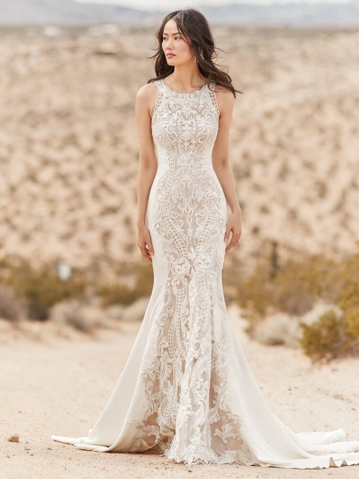 a woman standing in the sand wearing a wedding dress with an open back and high neck