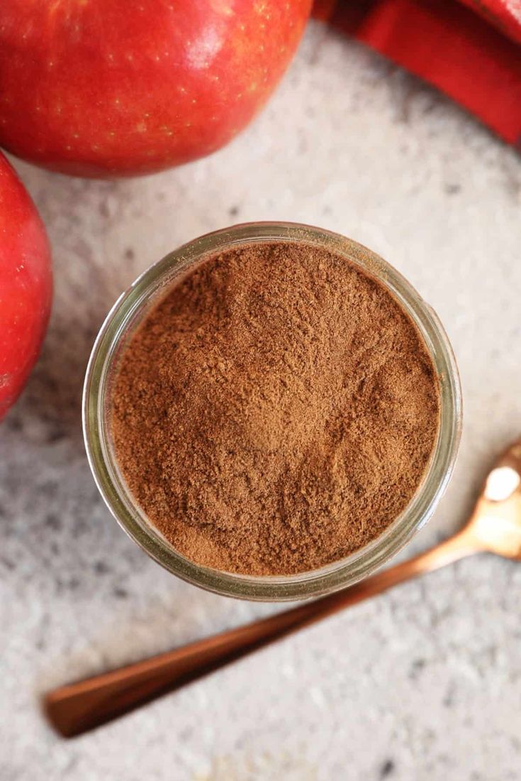 a glass jar filled with cinnamon powder next to apples