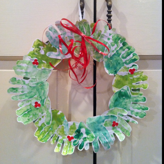 a christmas wreath hanging on the front door with red ribbon and holly leaves painted on it