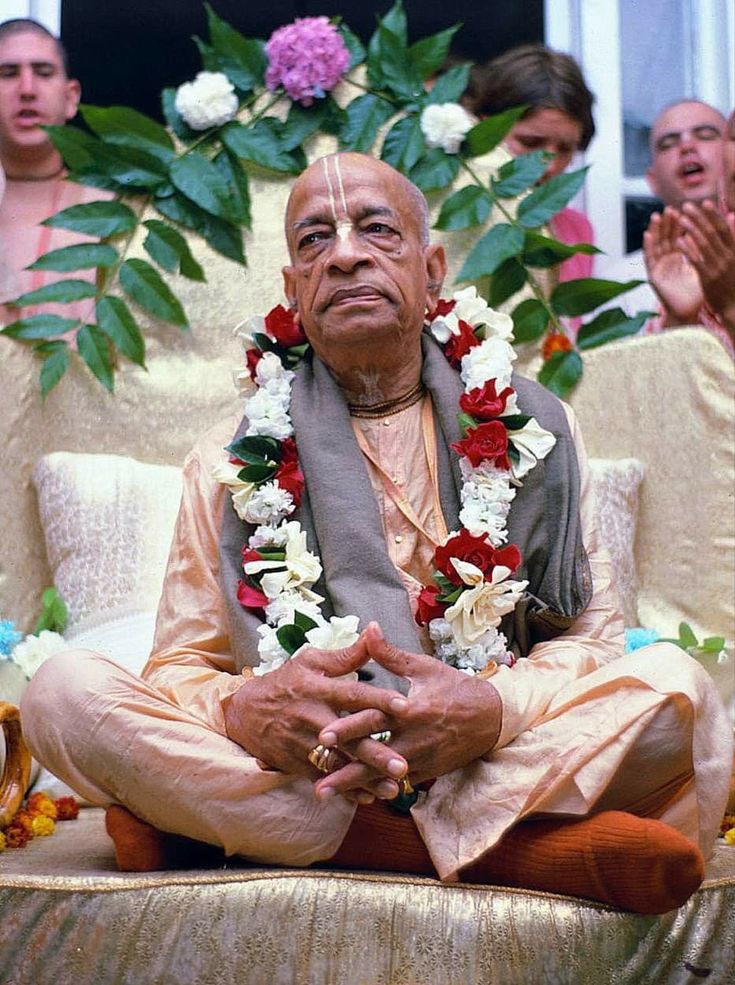 an old man sitting in a chair with flowers around his neck and hands clasped to his chest