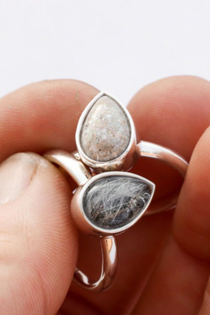 a person is holding a silver ring with two pieces of stone in it's middle