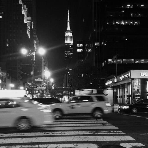 black and white photograph of cars driving down the street at night in new york city