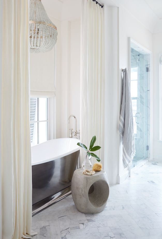 a white bath tub sitting under a window next to a plant in a glass vase