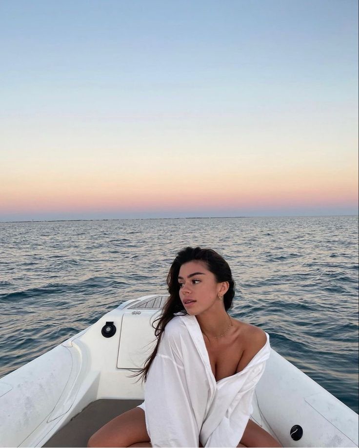 a woman sitting on the back of a boat in the middle of the ocean at sunset