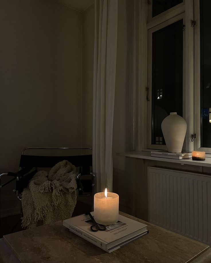 a lit candle sitting on top of a table next to a window