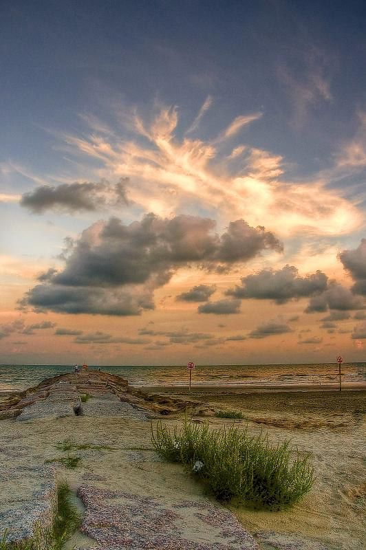 the sun is setting over an empty beach with rocks and grass in the foreground