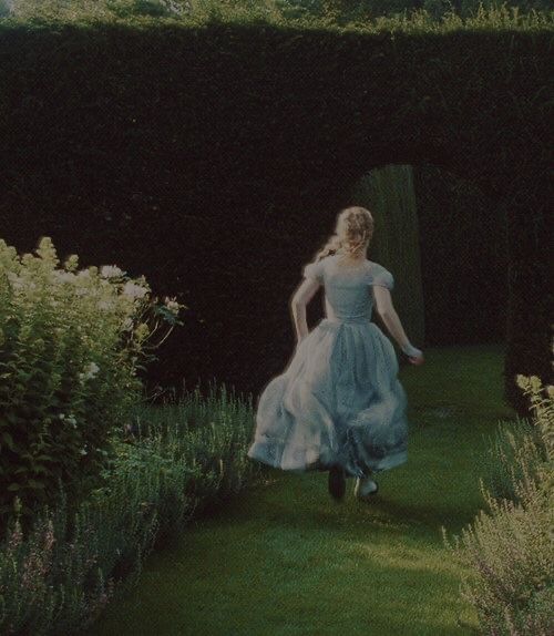 a woman in a blue dress walking through a garden