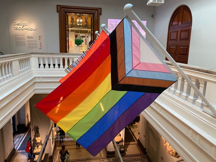 a large rainbow flag hanging from the side of a staircase in a building with white balconies