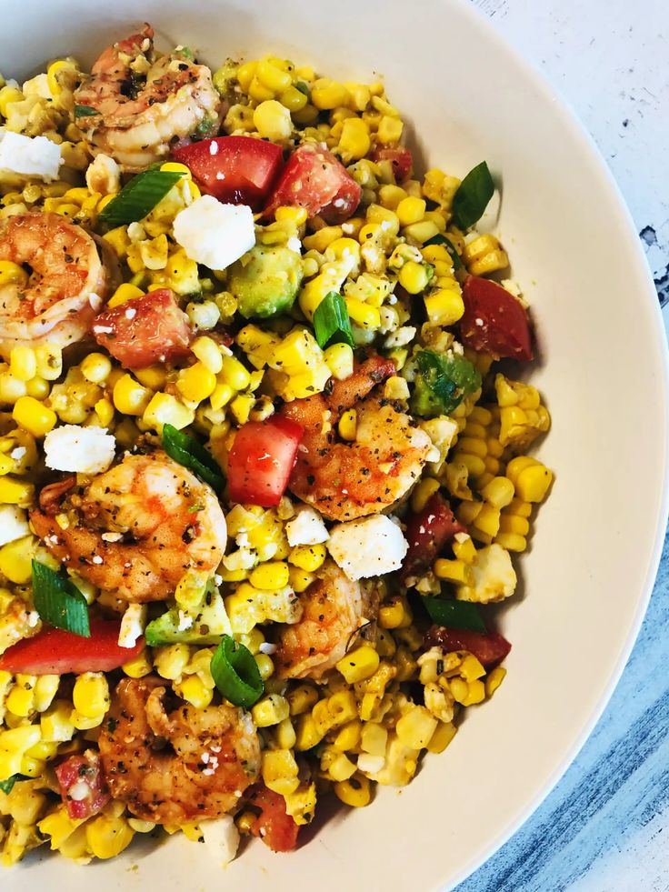 a white bowl filled with shrimp, corn and tomatoes on top of a blue table